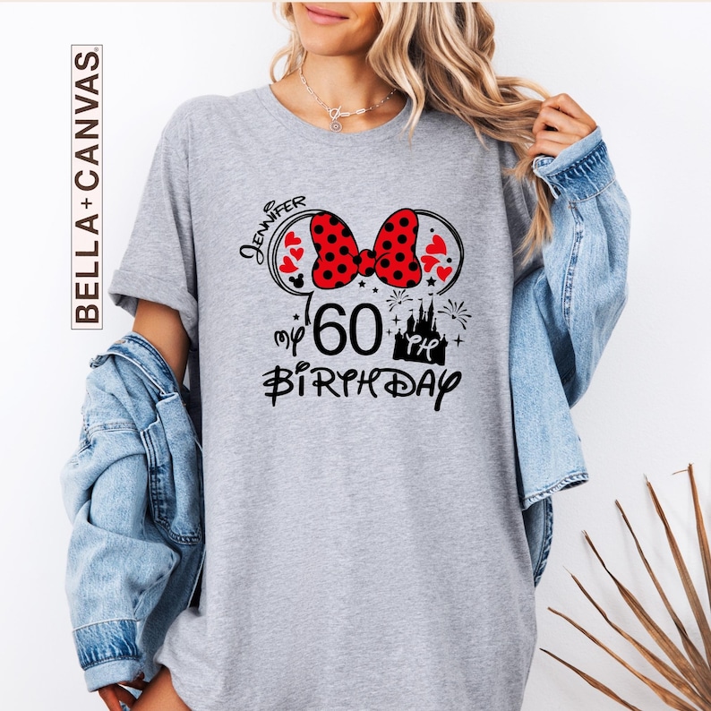 Puede incluir: Camiseta gris con un dise&ntilde;o inspirado en Minnie Mouse para un 60 cumplea&ntilde;os. El dise&ntilde;o incluye un lazo rojo de lunares, corazones, el nombre "Jennifer", un castillo y las palabras "my 60th Birthday" en negro.