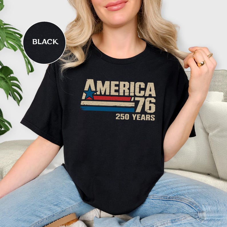 May include: Black t-shirt featuring the text "AMERICA '76 250 YEARS" in a retro design. The graphic includes a blue star and red and blue stripes. The shirt has a crew neck.