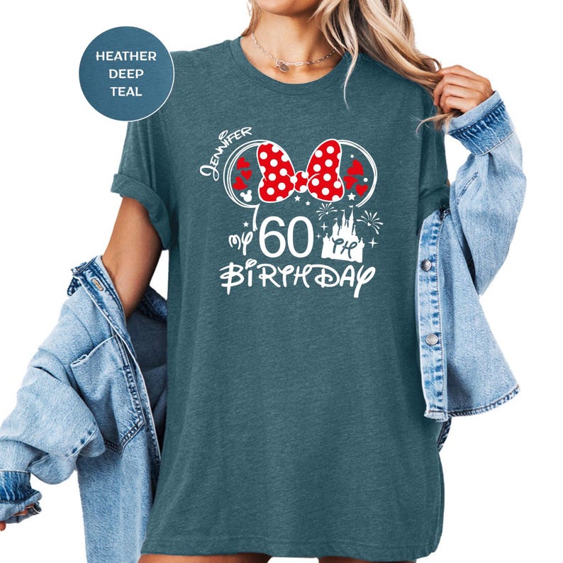 Puede incluir: Una camiseta de color verde azulado con un dise&ntilde;o gr&aacute;fico blanco que presenta un lazo rojo de lunares, el nombre "Jennifer", el n&uacute;mero "60" y las palabras "my birthday". La camiseta tiene las mangas enrolladas.