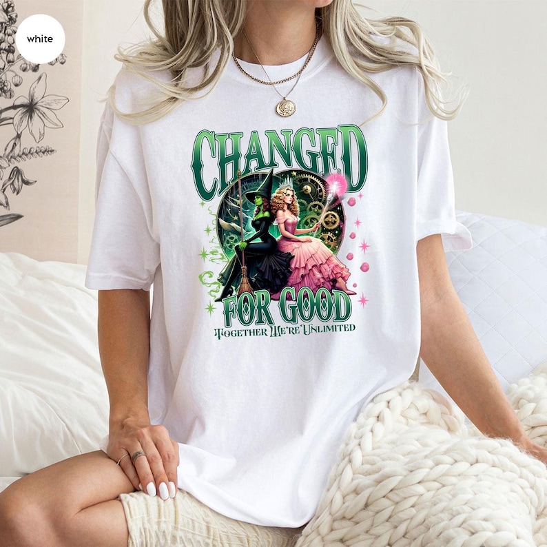 K&ouml;nnte beinhalten: Wei&szlig;es T-Shirt mit einem Grafikdesign aus dem Musical "Wicked". Das Design zeigt den Text "CHANGED FOR GOOD" und "TOGETHER WE'RE UNLIMITED". Das Kunstwerk zeigt die b&ouml;se Hexe des Westens und Glinda.