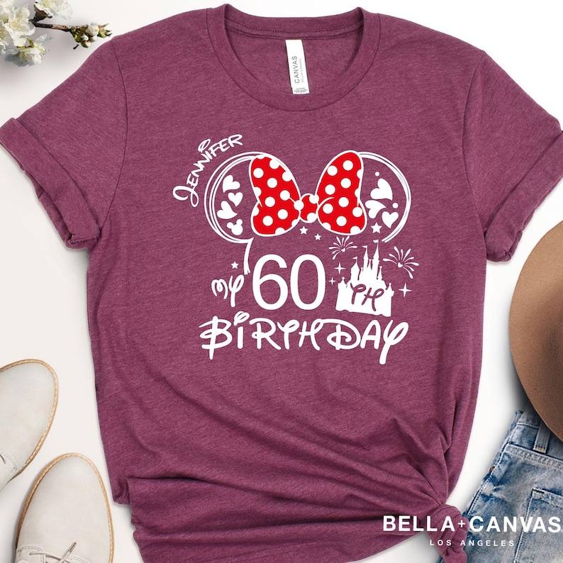 Puede incluir: Camiseta burdeos con un gr&aacute;fico blanco que presenta un lazo rojo de lunares, orejas de rat&oacute;n y el texto "Jennifer my 60th Birthday". La camiseta est&aacute; hecha de material suave y tiene mangas enrolladas.