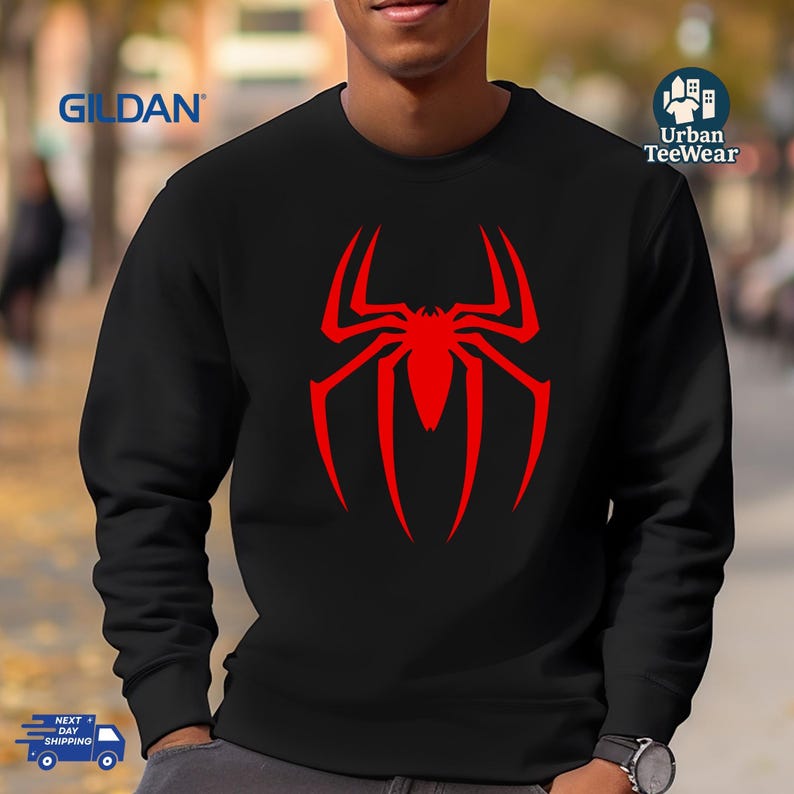 May include: Black sweatshirt with a large red spider logo on the front. The spider logo is a stylized design with long, curved legs and a central body. The sweatshirt has a crew neck and long sleeves. The brand name 'GILDAN' is printed on the upper left side.