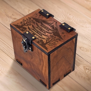 May include: A wooden box with a detailed laser-cut design of a Japanese pagoda, trees, and a mountain on the lid. The box is stained a warm brown color and features black metal hardware for the clasp and hinges. The box is rectangular.