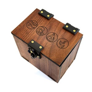 May include: A dark brown wooden box with engraved elemental symbols on the lid. The box has black hinges and a latch secured with gold-coloured screws. The design is symmetrical and the box is set against a white background.