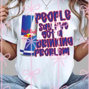 May include: White t-shirt featuring a Red Bull can graphic and the text "People Say I've Got a Drinking Problem" in red and blue. The shirt has short sleeves and a crew neck.