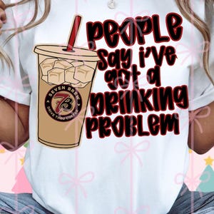 May include: White t-shirt with the phrase "People Say I've Got a Drinking Problem" in black and red lettering. The shirt features a graphic of an iced coffee drink with a red straw and the "Seven Brew" logo.