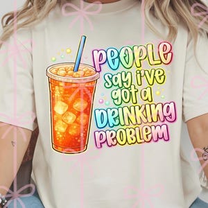 May include: Cream-colored t-shirt featuring a colorful graphic of a beverage in a clear plastic cup with ice cubes and a blue straw. The text reads "People say I've got a drinking problem."