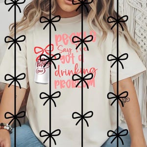 Könnte beinhalten: Cremefarbenes T-Shirt mit dem Text "People Say I've Got a Drinking Problem" in rosa und roter Schrift. Eine Dose Diet Dr. Pepper ist auf dem Shirt abgebildet. Das Shirt hat kurze Ärmel.