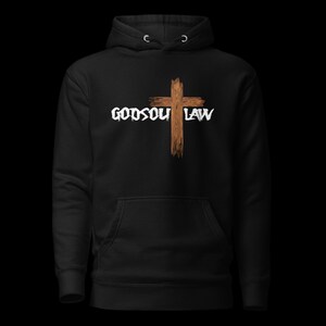 Op de afbeelding: Zwarte hoodie met een voorzak en een capuchon met trekkoord. Het ontwerp toont een bruin kruis en de witte woorden "GODSOUL LAW". De hoodie is gemaakt van een zacht materiaal.