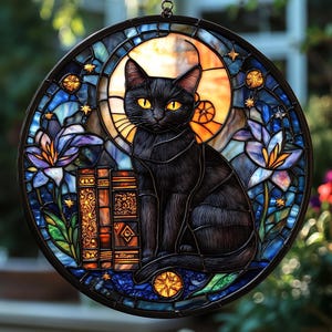 Pode incluir: Vitral redondo com um gato preto de olhos amarelos em frente a uma lua. O vitral, com moldura escura, inclui livros, flores e estrelas em tons de azul, laranja e amarelo.