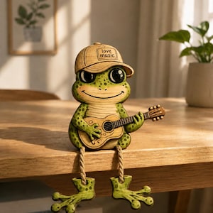 May include: A whimsical frog figurine with a guitar, wearing a cap that says "love music." The frog is green with black eyes and sits on a wooden table. Its legs dangle over the edge. A charming decorative piece.