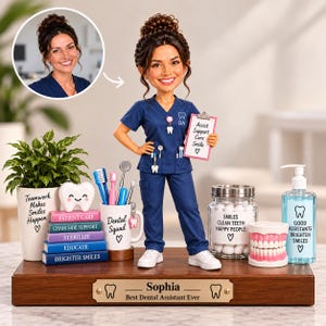 Op de afbeelding: Een op maat gemaakte bobblehead-figuur van een tandartsassistent in marineblauw uniform met een klembord waarop staat Assist Support Care Smile. De basis heeft een plaatje met de naam Sophia en de tekst Best Dental Assistant Ever.
