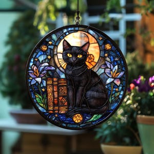 Pode incluir: Janela redonda de vitral com um gato preto de olhos amarelos, sentado em frente a uma pilha de livros. O design inclui uma lua, estrelas e flores azuis e roxas. A janela &eacute; emoldurada em preto.