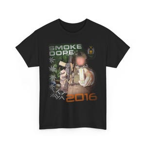 Könnte beinhalten: Schwarzes T-Shirt mit einem Grafikdesign. Das Design enthält die Wörter "SMOKE DOPE" in Weiß und Grün, ein Bild einer Person, die ein Gewehr und ein Paket hält, und die Zahl "2016" in Orange.