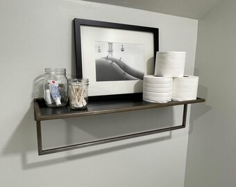 Può includere: Una mensola in metallo con un quadro con cornice in bianco e nero, due barattoli di vetro e diversi rotoli di carta igienica bianca. Un barattolo contiene cotton fioc e l'altro dentifricio e articoli da toeletta.