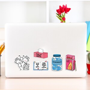 May include: A white laptop with six colorful stickers. The stickers feature illustrations and text. One sticker says "If my book is open, your mouth should be closed". Another sticker says "Crying over fictional characters".