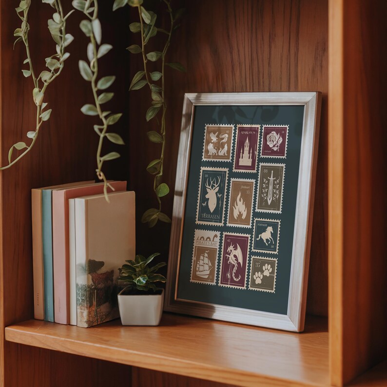 May include: A framed print featuring postage stamp designs with various illustrations, including a deer, a flame, a sword, and a dragon. The frame is silver, and the print is displayed on a wooden shelf with books and a small potted plant.