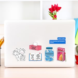 May include: A laptop computer with several stickers on it. The stickers are colorful and feature various designs and text, including "Crying over fictional characters", "If my book is open, your mouth should be closed", "Antidepressants", "Slow Burn", and "Sorry I can't, the enemies just became lovers."