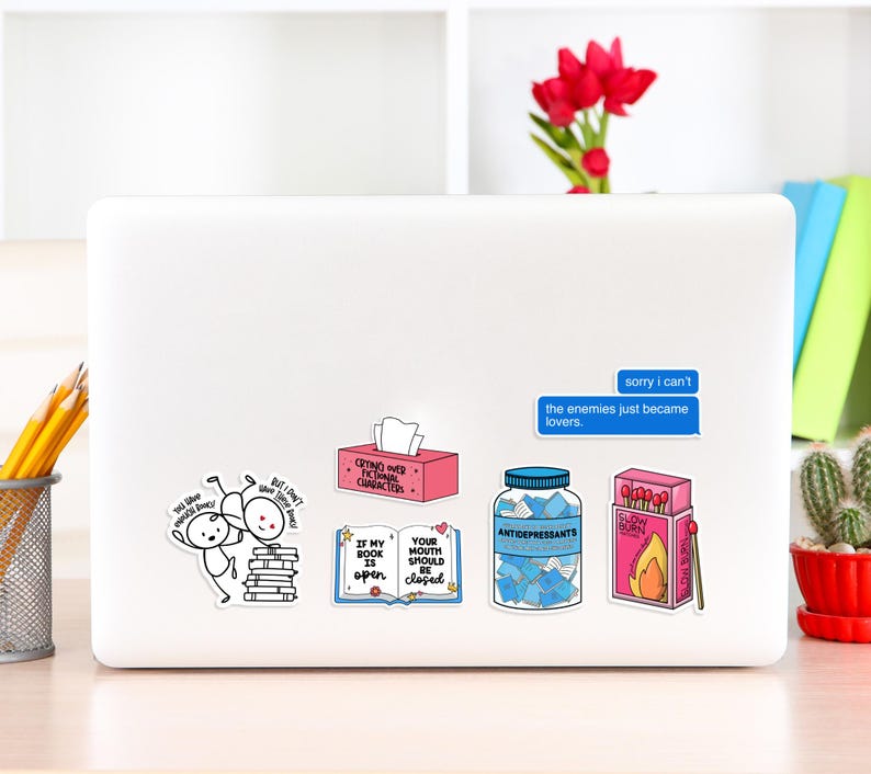 May include: A laptop computer with several stickers on it. The stickers are colorful and feature various designs and text, including "Crying over fictional characters", "If my book is open, your mouth should be closed", "Antidepressants", "Slow Burn", and "Sorry I can't, the enemies just became lovers."
