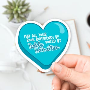 May include: A blue heart-shaped sticker with the text "May all your book boyfriends be voiced by Teddy Hamilton".