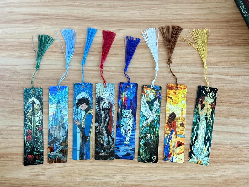 May include: A collection of eight rectangular bookmarks with colorful illustrations and matching tassels. The designs include a sword, a castle, a figure in blue, a dragon, a white tiger, a bird, a woman, and a woman with a flower.