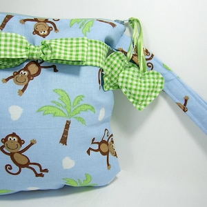 May include: A light blue zippered pouch with a green and white gingham bow and a matching strap. The pouch is decorated with a pattern of brown monkeys and green palm trees.