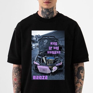 May include: Black short-sleeved t-shirt featuring a graphic of a car with its hood open, showcasing the engine. The image includes the text "KING OF THE SPEEDZ" and "82022" in a purple font. The shirt has a crew neck.