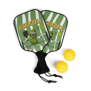 Peut inclure: Deux raquettes de pickleball avec un motif à rayures vertes et blanches et le mot "PICKLEBALL" en jaune. Les raquettes présentent un personnage de cornichon de dessin animé jouant au pickleball. Deux balles de pickleball jaunes sont également incluses.