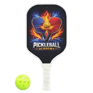 May include: A pickleball paddle with a black face featuring a design of two paddles, a ball, and flames. The text "Pickleball Academy" is displayed below the paddles. A yellow pickleball is next to the paddle.