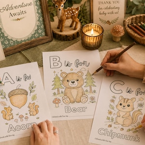 Woodland baby shower ABC book activity printable featuring guests coloring alphabet pages at a cozy baby shower table. Includes woodland animal coloring sheets, baby shower keepsake activity, printable ABC book game, forest theme baby shower decor, and gender neutral baby shower activity with colored pencils and rustic woodland decorations.
