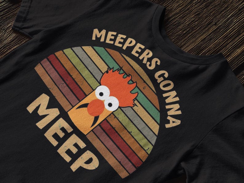 Peut inclure: T-shirt noir avec un personnage de dessin anim&eacute; aux cheveux orange et au nez rouge, sur un fond arc-en-ciel r&eacute;tro. Le texte "MEEPERS GONNA MEEP" est inscrit en arc au-dessus et en dessous du personnage.