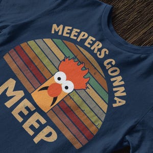 Peut inclure: T-shirt bleu marine avec un motif r&eacute;tro d'un personnage de Muppet et le texte "MEEPERS GONNA MEEP". Le motif comprend un arc-en-ciel color&eacute;.