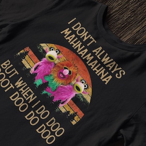Könnte beinhalten: Schwarzes T-Shirt mit einem Retro-Design, das drei Muppet-Charaktere und den Text "I DON'T ALWAYS MAHNA MAHNA BUT WHEN I DO DO DOOT DOO DO DOO" zeigt. Die Charaktere sind rosa, orange und grün, vor einem Sonnenuntergang.