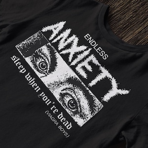 May include: Black t-shirt with a white graphic design. The design features the word "ANXIETY" in a distressed font, the words "ENDLESS" and "sleep when you're dead" and a close-up of two eyes. The text "(VIAGRA BOYS)" is also included.