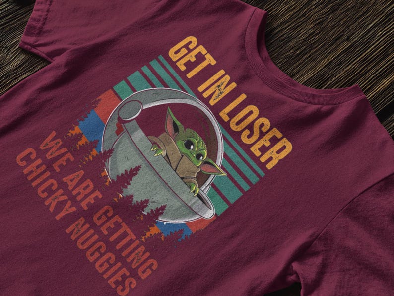 K&ouml;nnte beinhalten: Burgunderfarbenes T-Shirt mit einer Grafik von Grogu aus The Mandalorian in einer Kapsel, mit dem Text "GET IN LOSER WE ARE GETTING CHICKY NUGGIES". Das Design beinhaltet ein Retro-Farbschema und Waldmotive.