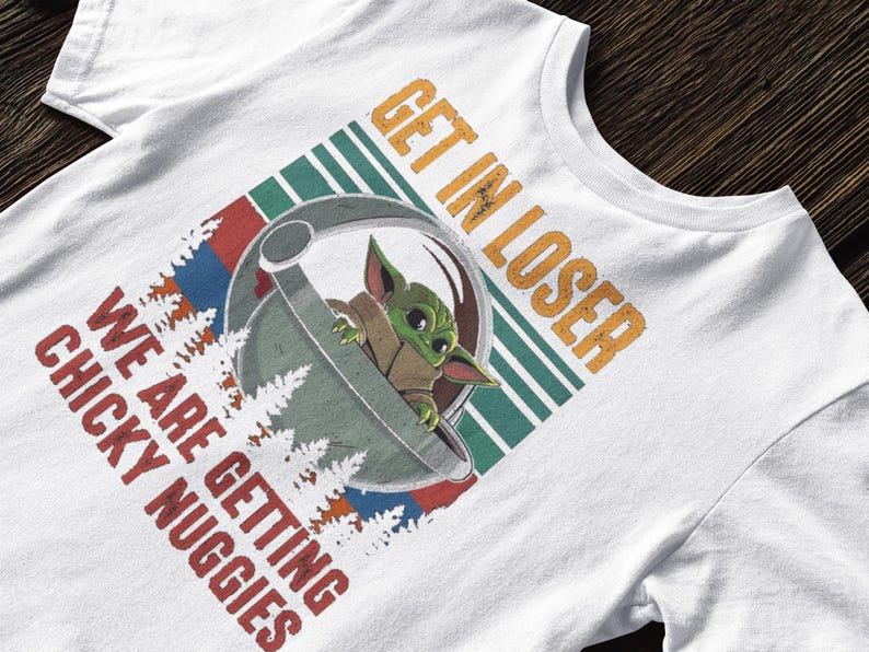 K&ouml;nnte beinhalten: Wei&szlig;es T-Shirt mit einer Grafik eines gr&uuml;nen Alien-Charakters in einer Kapsel und dem Text "GET IN LOSER WE ARE GETTING CHICKY NUGGIES" in Orange und Rot. Das Design hat einen Retro-Stil mit gr&uuml;nen und blauen Streifen.
