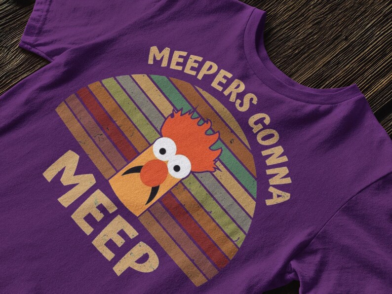 Peut inclure: T-shirt violet avec un graphisme de Beaker des Muppets. Le design comprend le texte "MEEPERS GONNA MEEP" dans un style r&eacute;tro, avec un fond ray&eacute; color&eacute; derri&egrave;re Beaker.