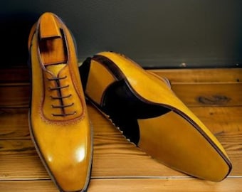 May include: A pair of yellow leather lace-up shoes with black leather accents on the soles. The shoes have a pointed toe and a polished finish.