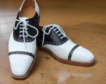 May include: A pair of black and white leather shoes with a saddle design. The shoes have a lace-up closure and a rounded toe.