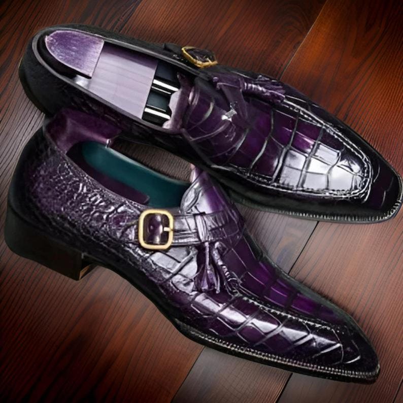 May include: A pair of purple leather dress shoes with a crocodile pattern. The shoes feature a tassel detail and a buckle closure.