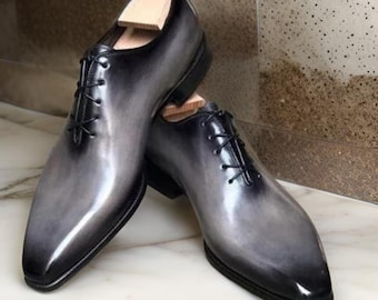 Puede incluir: Un par de zapatos de cordones de cuero negro con un degradado de negro a gris. Los zapatos tienen una punta puntiaguda y un acabado pulido.