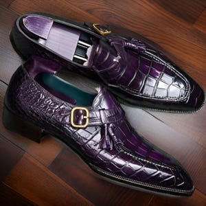 May include: A pair of purple leather dress shoes with a tassel detail and a buckle fastening. The shoes have a crocodile-embossed pattern.