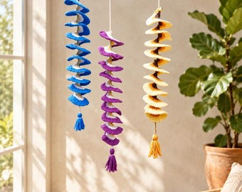 May include: Three hanging spiral decorations made of crocheted yarn. The left spiral is blue and white, the center is purple and white, and the right is yellow and brown. Each spiral features a matching yarn tassel at the bottom end.