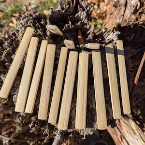 May include: A collection of light-colored, rectangular wooden pieces, possibly craft sticks or small slats, arranged on a textured, dark brown surface. The pieces are uniform in size and shape, with a natural wood grain.