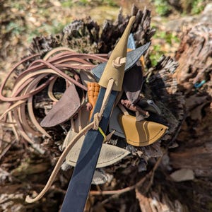 May include: A black bow with a tan leather grip and a tan leather tip. The bow is surrounded by various leather pieces in shades of brown and tan. The bow is resting on a weathered wooden surface.