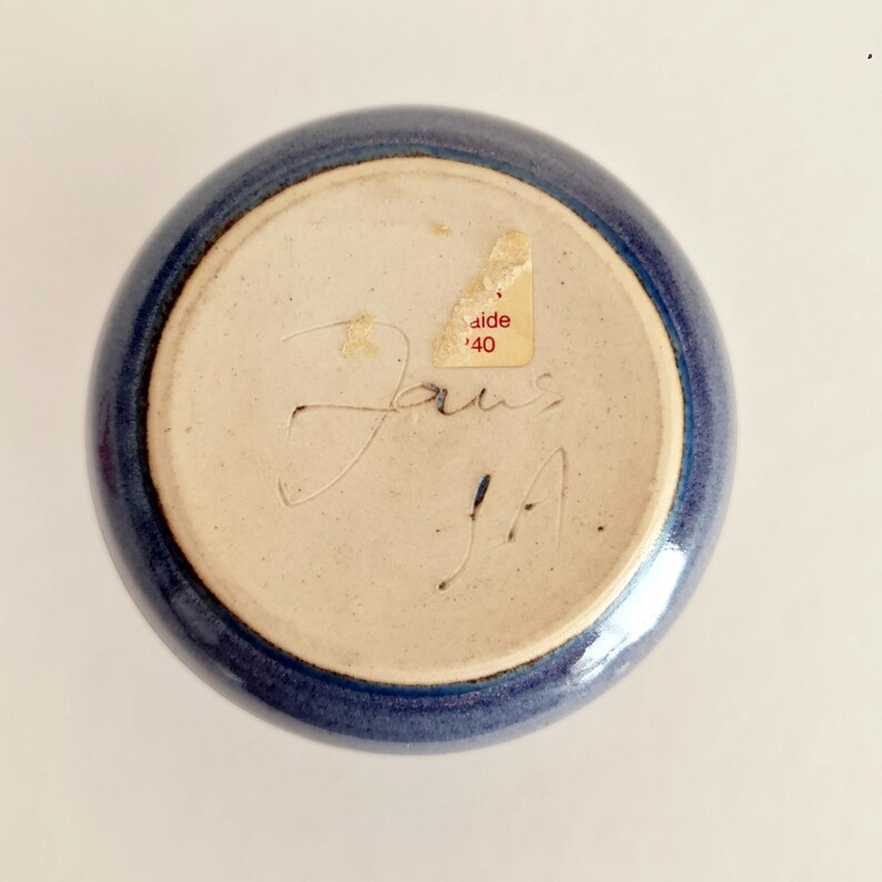 Pu&ograve; includere: Una ciotola di ceramica blu con interno beige chiaro. Il fondo della ciotola presenta firme manoscritte e un adesivo con la scritta "aide '40". La ciotola ha una forma rotonda e una finitura lucida.