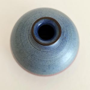 Pu&ograve; includere: Un vaso di ceramica blu con corpo rotondo e collo stretto. Il vaso ha un bordo marrone scuro e un interno blu. Il fondo del vaso ha una tonalit&agrave; rosso-rosata. Il vaso &egrave; probabilmente fatto a mano e ha una superficie strutturata.