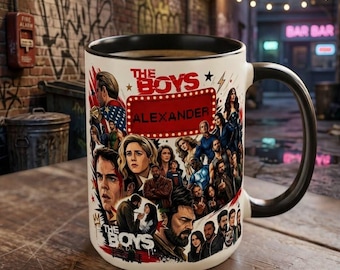 May include: A white ceramic mug with a black handle and interior, featuring a colorful graphic collage of characters from the television series The Boys, with the text The Boys and the name Alexander printed in a red rectangular frame on the front.