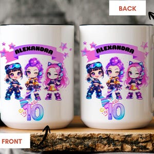 May include: A white ceramic mug with a black handle and rim, featuring a graphic of three chibi-style characters, pink stars, a pink banner with the name ALEXANDRA, and a large number 10 in blue and purple gradient colors with a party hat icon.