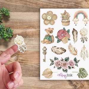May include: A sheet of stickers featuring a variety of illustrations, including a teddy bear, flowers, feathers, dreamcatchers, a key, a rainbow, and a potted plant. The stickers are on a white background and have a whimsical, boho aesthetic. The text "Whimsy Ink" is printed in the bottom right corner.
